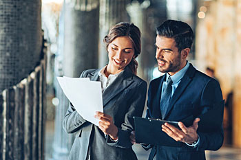 Master Studentin und Student im Business Look besprechen Bilanzen im Flur des Unternehmens