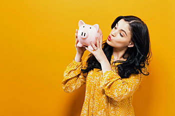 Junge Frau haelt ein Sparschwein in der Hand und gibt ihm einen Kuss