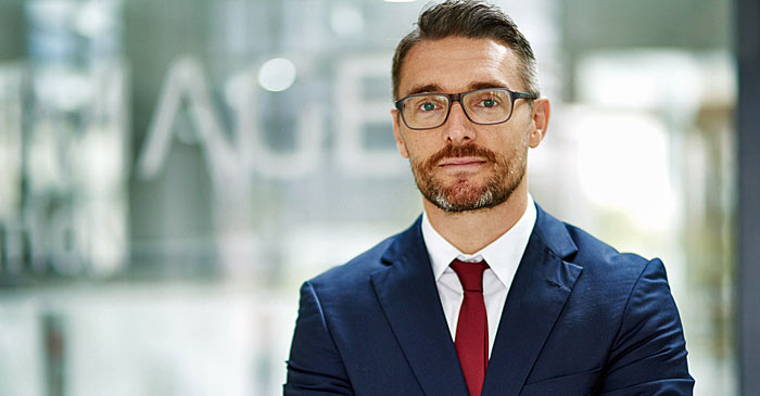 Junger Mann im Anzug steht vor der Glastuer seines Bueros