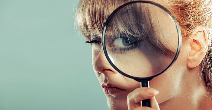 Junge Frau haelt eine Lupe an ihr Auge und blickt hindurch