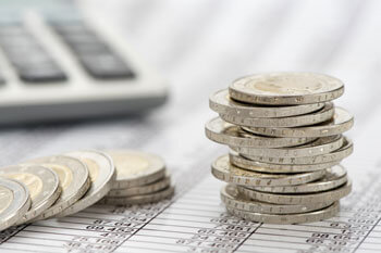 Kleingeld liegt aufeinander gestapelt und zerstreut auf einem Dokument neben einem Taschenrechner